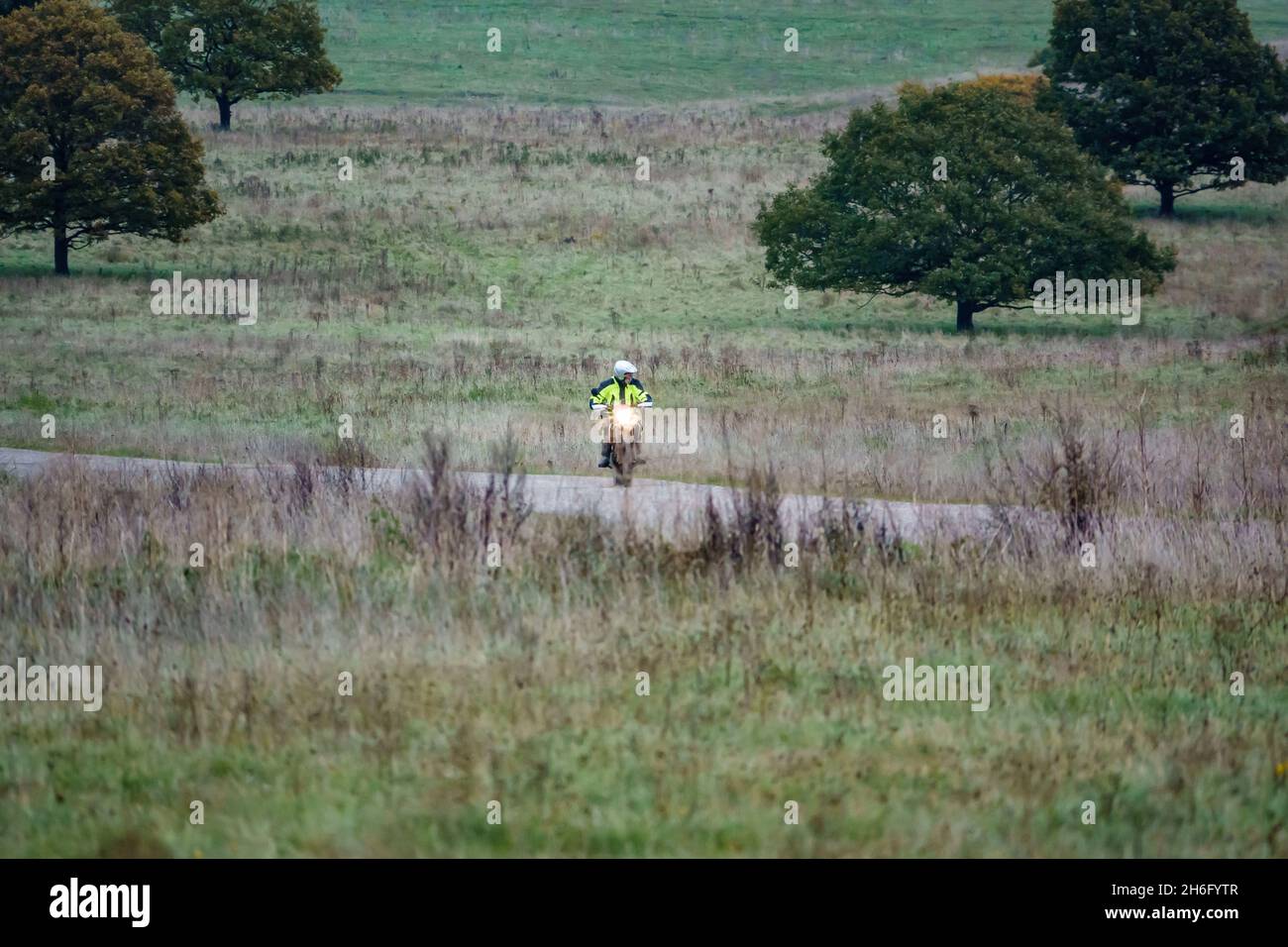 Ein Motorradfahrer (Biker) in einer gelben Jacke, der mit seinem Motorrad auf einem Steinweg auf der Salisbury Plain, Wiltshire, fährt Stockfoto