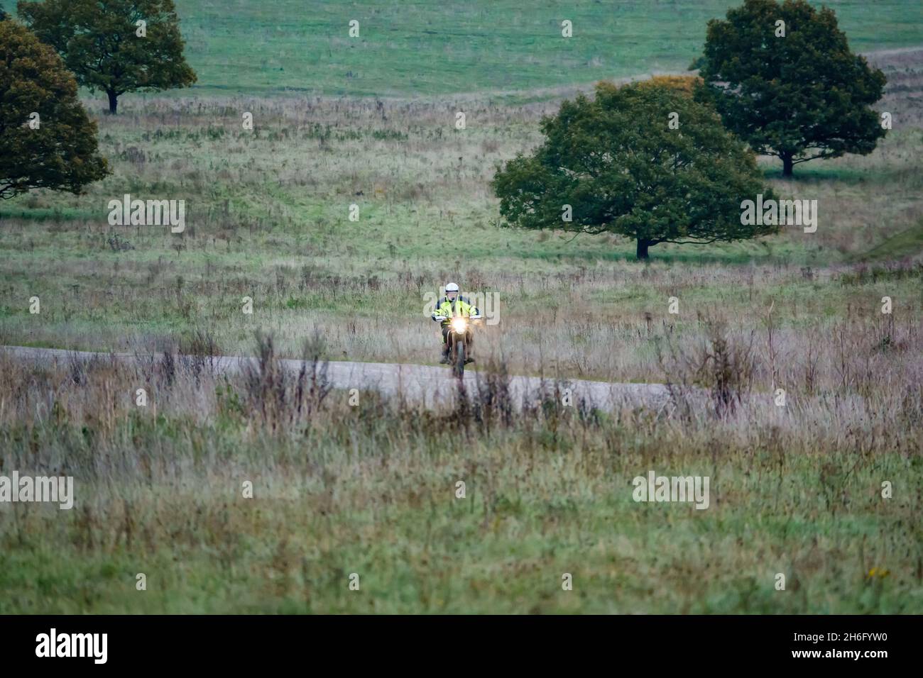 Ein Motorradfahrer (Biker) in einer gelben Jacke, der mit seinem Motorrad auf einem Steinweg auf der Salisbury Plain, Wiltshire, fährt Stockfoto