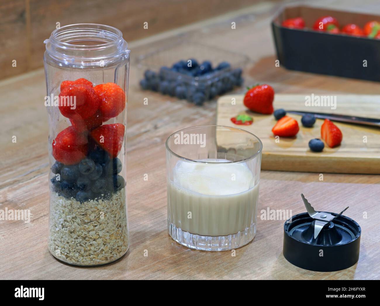 Smoothie-Mixer gefüllt mit frischem, gesundem Obst und Haferflocken, fertig zum Mischen mit Milch auf einem Holztisch Stockfoto