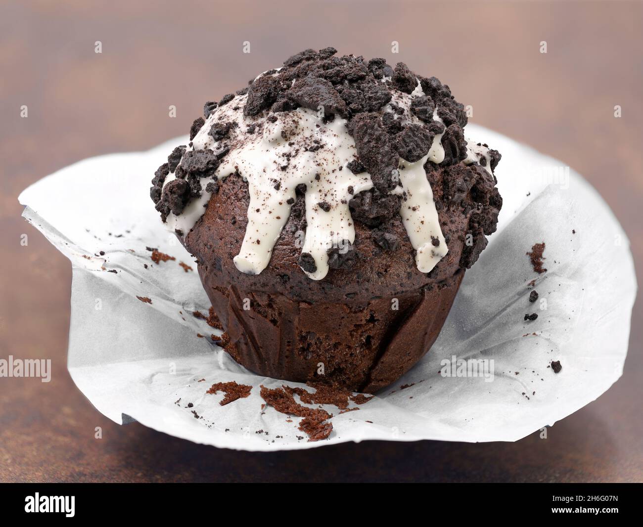 Schokoladenmuffin mit weißer Glasur und dunklen Keksbröseln auf braunem Hintergrund, ausgepackter Cupcake Stockfoto