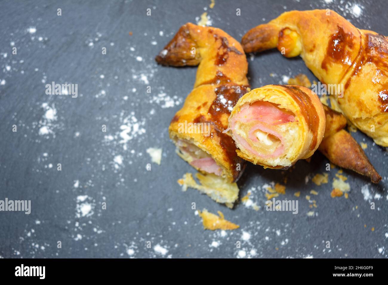 Frisch gebackene Croissants, gefüllt mit Schinken und geschmolzenem Käse, verzehrfertig, auf einem grauen Schieferteller Stockfoto