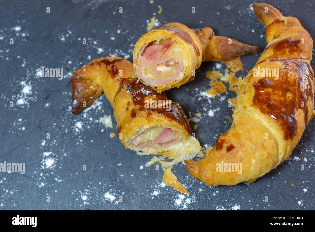Frisch gebackene Croissants, gefüllt mit Schinken und geschmolzenem Käse, verzehrfertig, auf einem grauen Schieferteller Stockfoto
