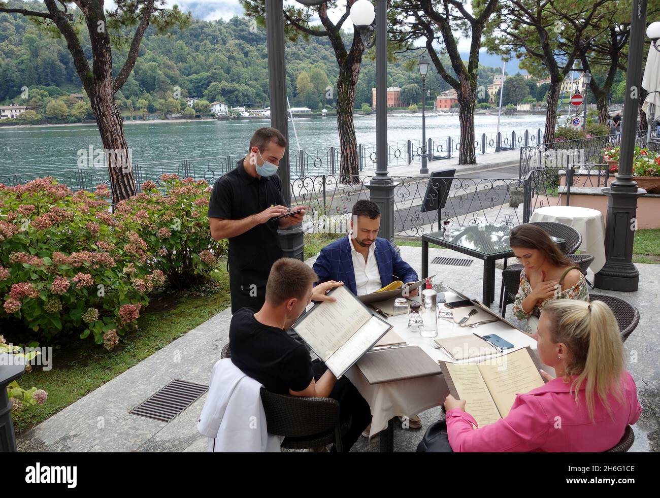 Der Kellner im Restaurant nimmt Bestellungen von den Gästen im Lenno am Comer See, Italien, an Stockfoto