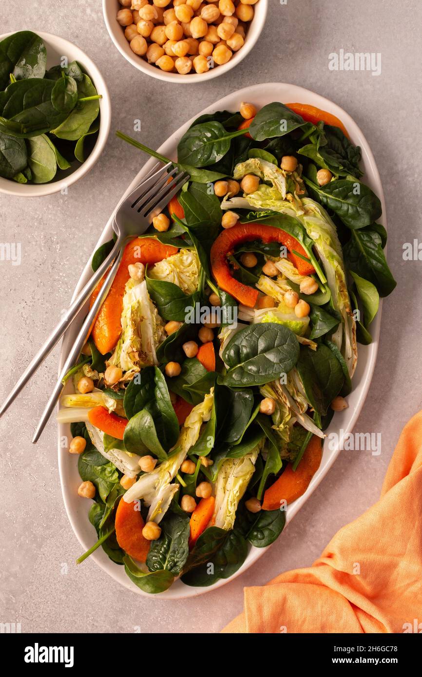 Gesunder, köstlicher vegetarischer Salat aus Spinat und Kichererbsen, gebackenem Kürbis und Chinakohl, Draufsicht auf ein ovales Gericht mit Salat Stockfoto