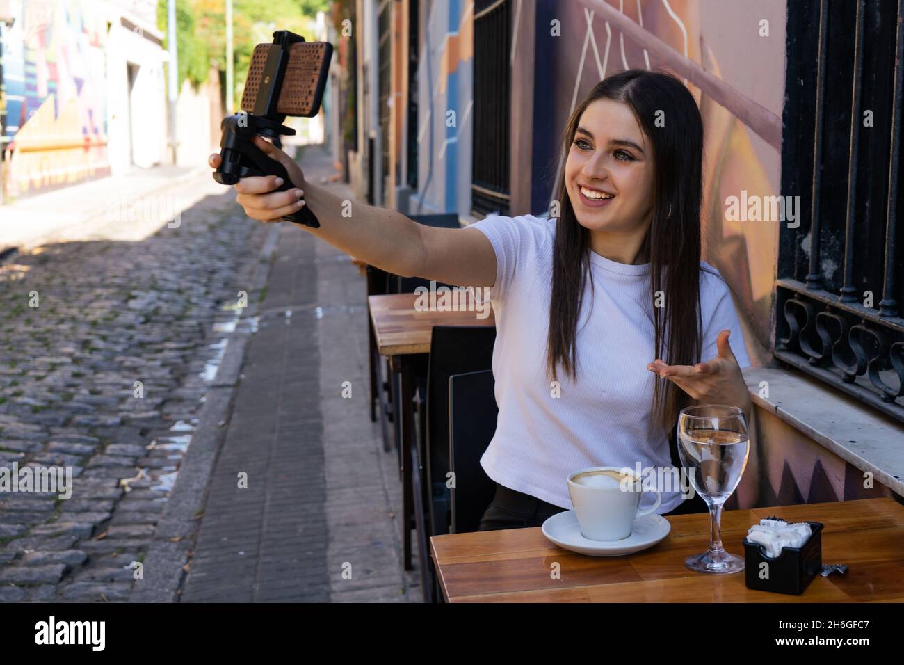 Schöne Latina Influencerin mit grauen Augen, die einen Videobeitrag mit ihrem Handy aufzeichnete, um sie in soziale Netzwerke hochzuladen. Visuelles Kommunikationskonzept, Stockfoto