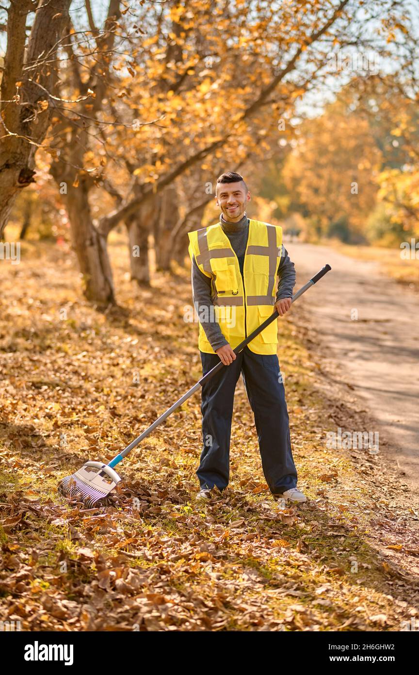 Ein Mann in einer gelben Weste, der Blätter im Park abhakt Stockfoto