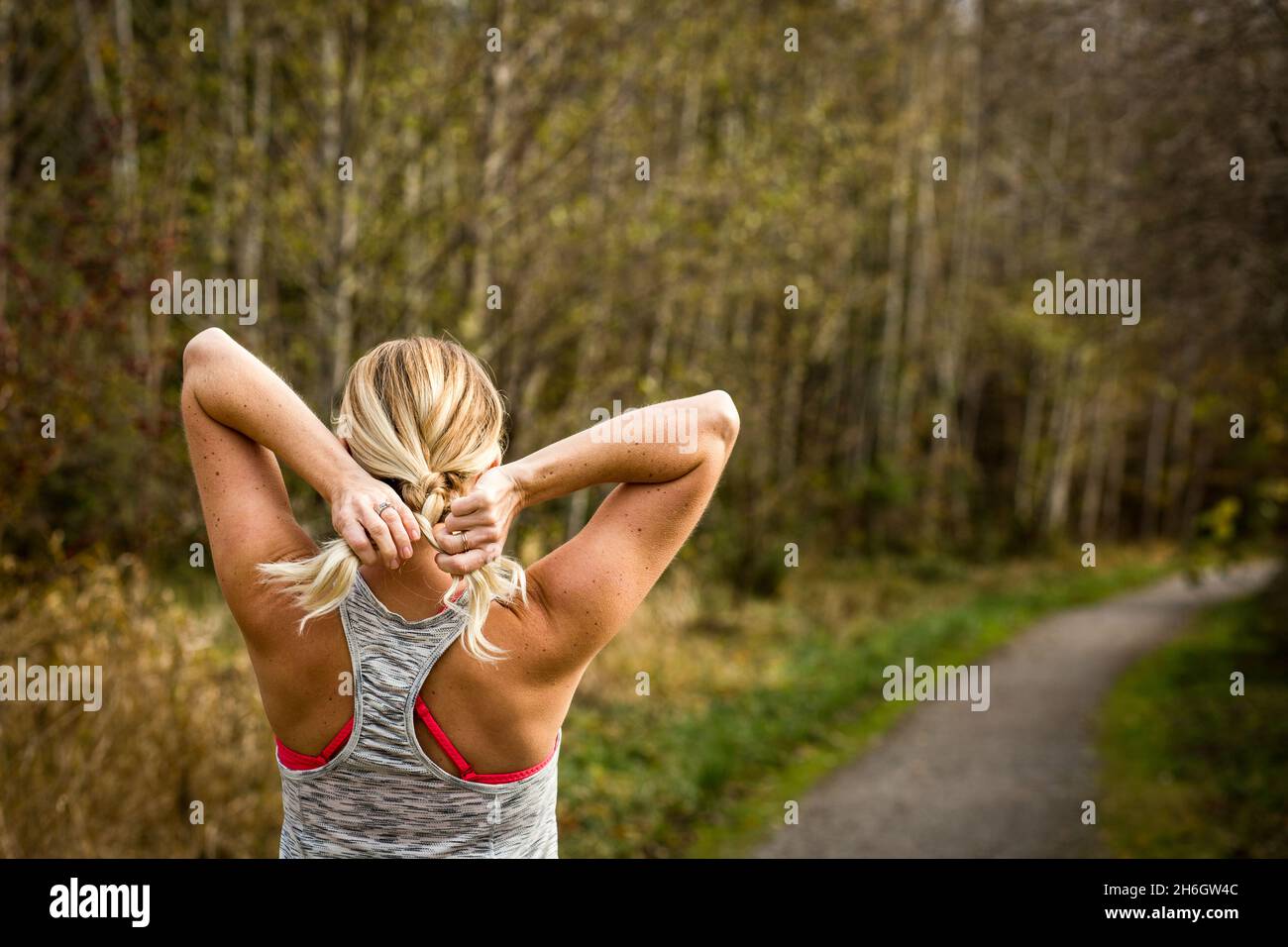 Frau in Trainingsbekleidung flechst Haare auf dem Trail Stockfoto