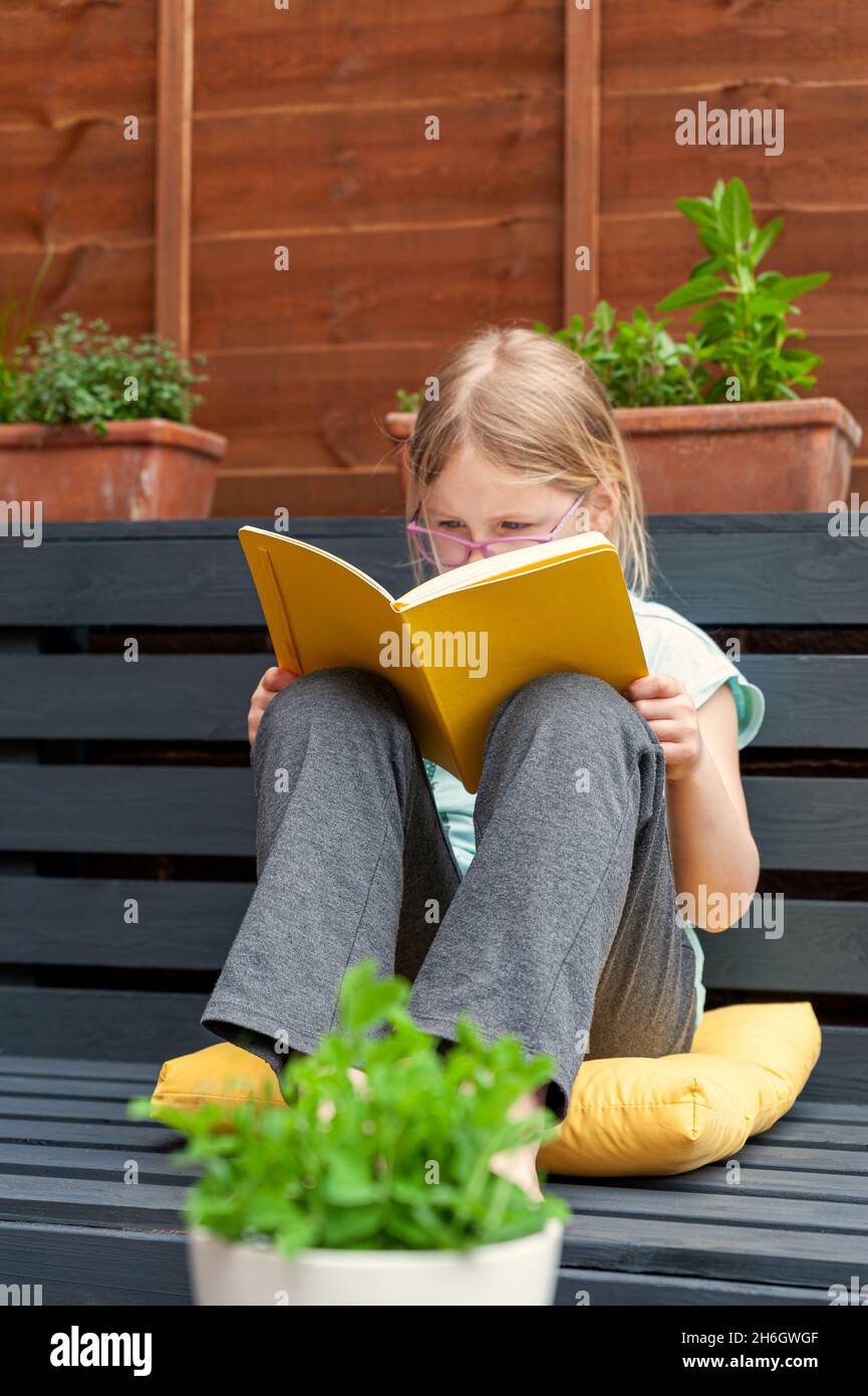 Kleines Mädchen, das im Garten sitzt und Vorbereitungsarbeiten für ihre Schule macht. Stockfoto