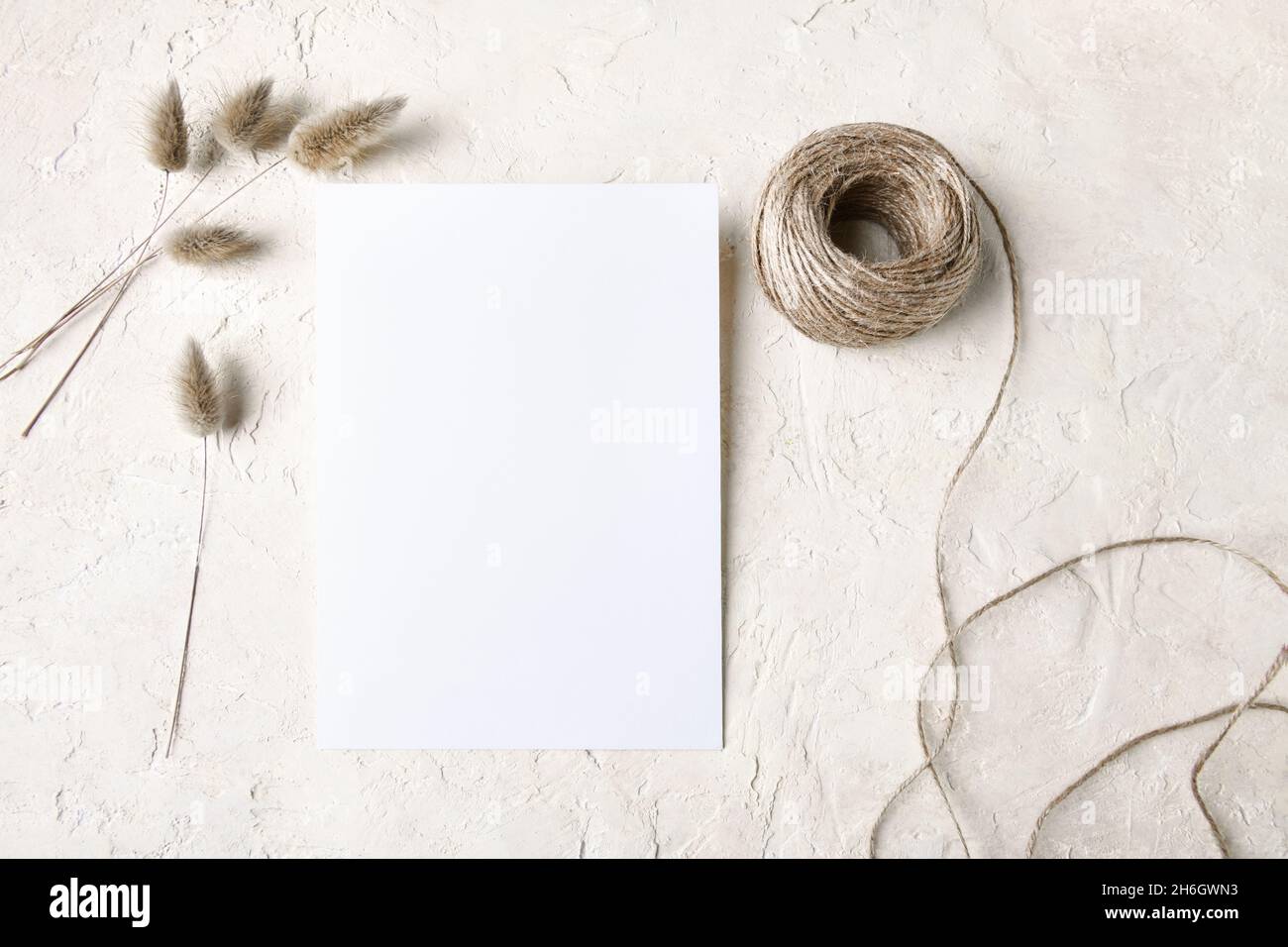 Weißes Einladungskartenmockup mit Boho-Dekoration: Trockenes Gras und Seil, natürliches umweltfreundliches Dekor, minimalistisches Mockup 5x7-Verhältnis, ähnlich A6, A5 Stockfoto