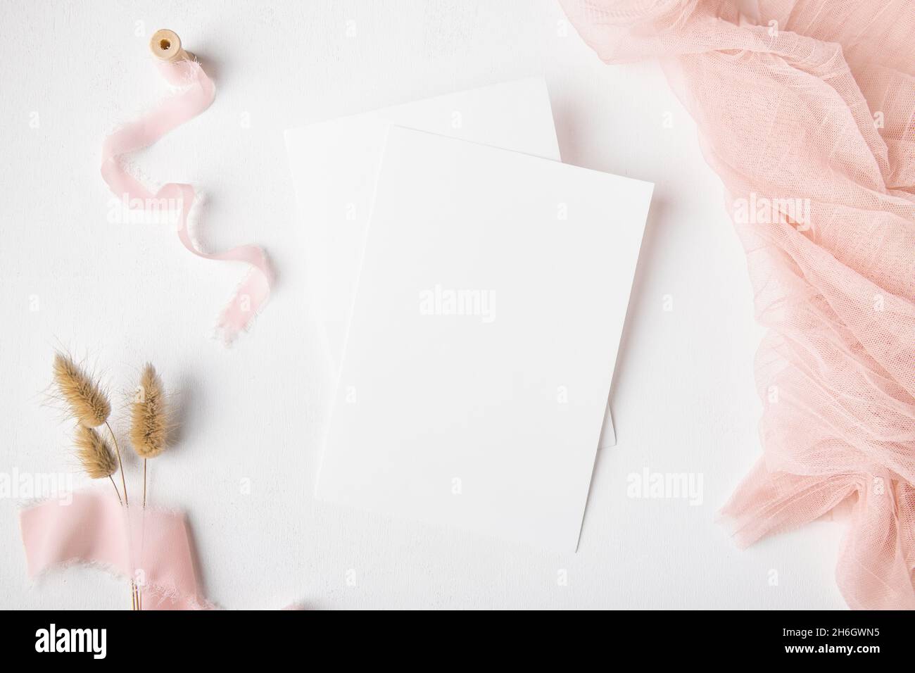 Zwei weiße Hochzeit Einladung Karte mockup auf weißem Tischhintergrund mit rosa Terrakotta-Dekoration und trockenem Gras, minimalistisches mockup 5x7 Verhältnis, ähnlich Stockfoto