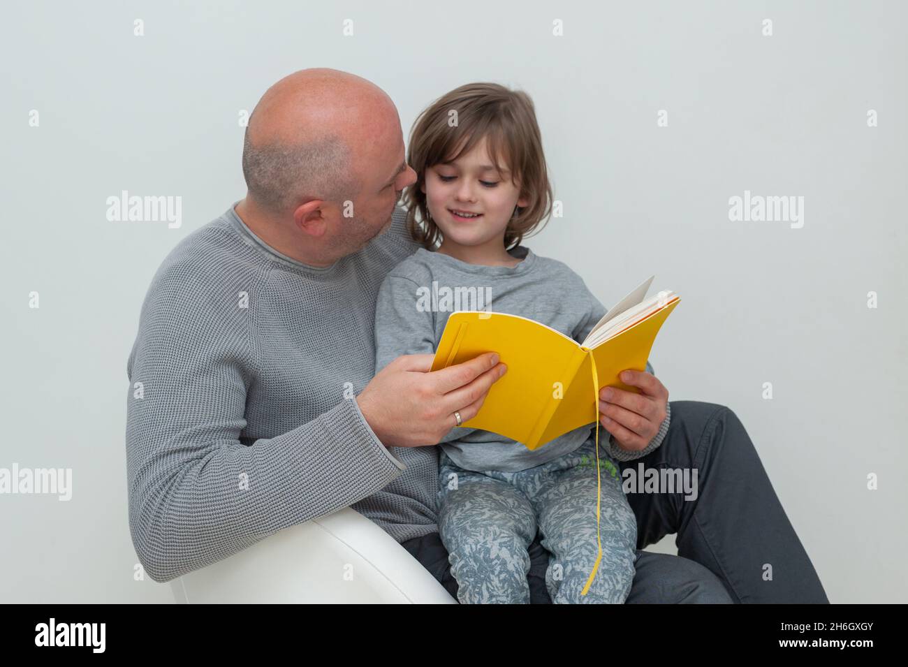 Vater und Sohn genießen zusammen das Lesen und diskutieren Schulaufgabenübungen aus gelbem Lehrbuch. Stockfoto