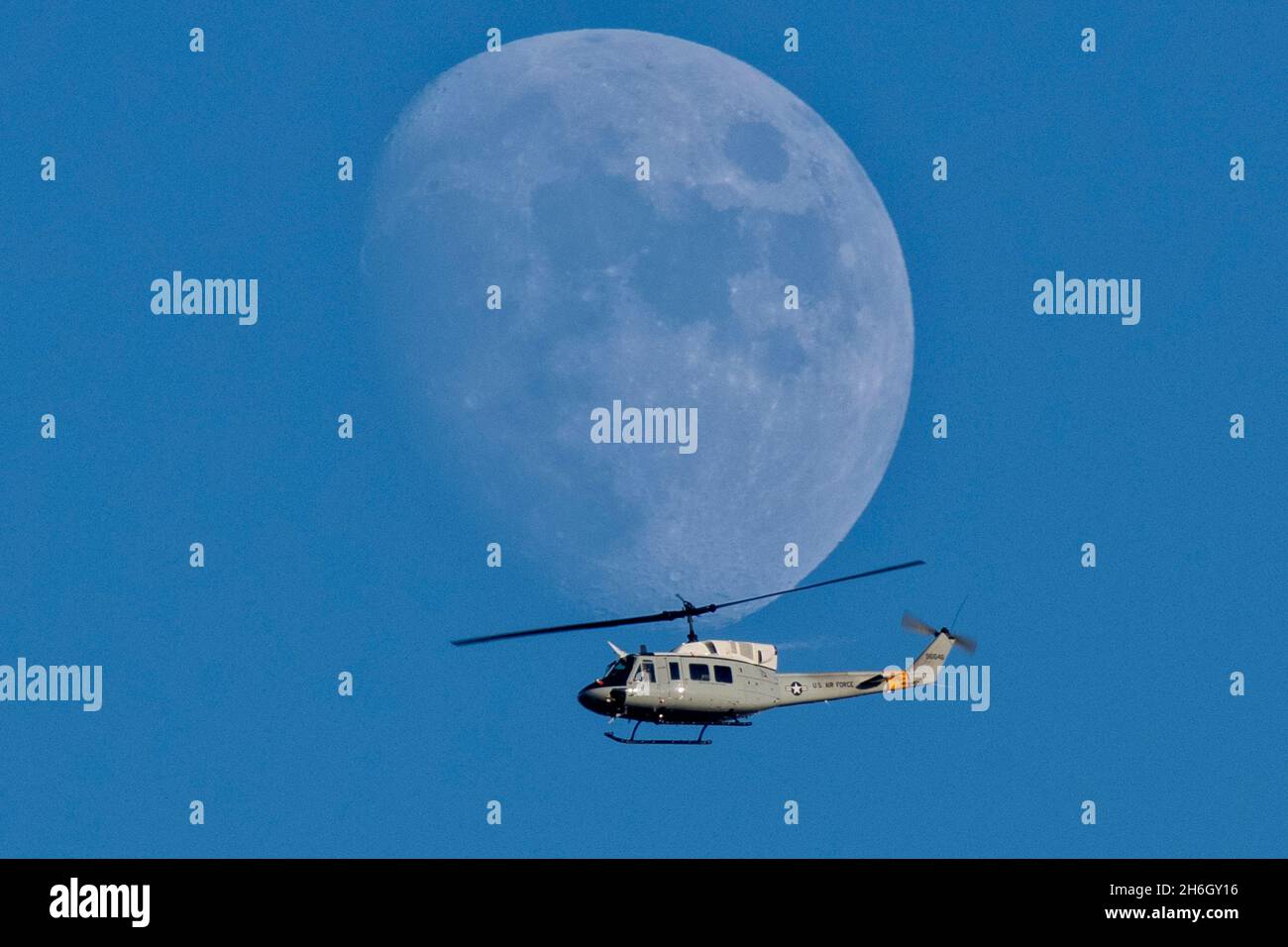 Yokota, Japan. März 2021. Während einer Trainingsmission über der Yokota Air Base am 15. November 2021 in Yokota, Japan, fliegt ein zunehmend krautiger Mond, der bei Tageslicht als Hubschrauber der US Air Force UH-1N Iroquois beleuchtet wird, der dem 459. Airlift Squadron zugewiesen wurde. Kredit: Osakabe Yasuo/U.S. Air Force/Alamy Live News Stockfoto