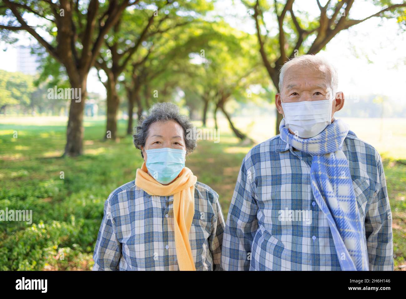 Asiatisches Senior-Paar in medizinischer Maske und Herbstkleid zu Fuß im Park Stockfoto