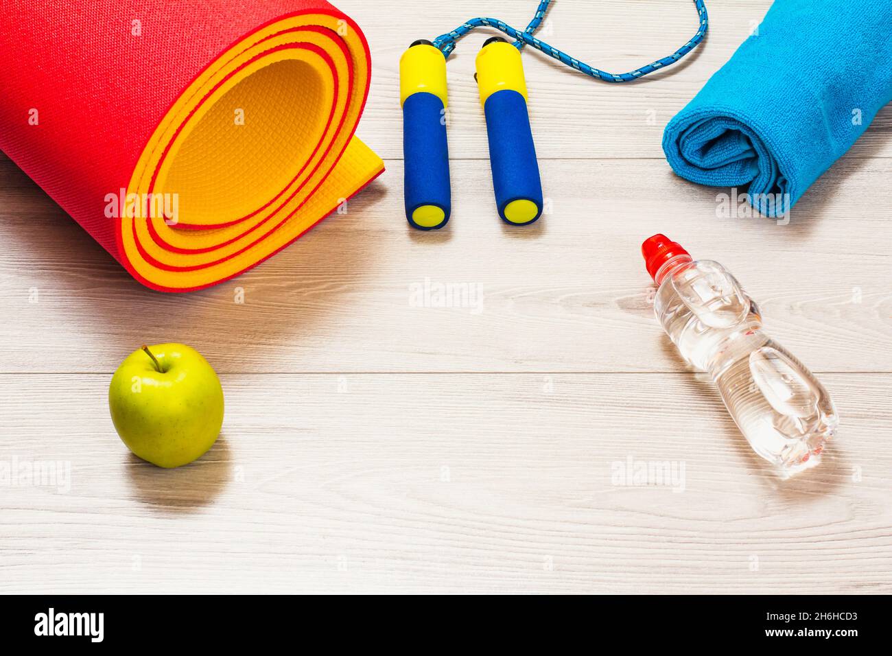 Yogamatte und Skippergrube für Fitness, ein Handtuch, eine Flasche Wasser, einen Apfel in einem Raum oder ein Fitnessstudio auf dem grauen Boden. Stockfoto