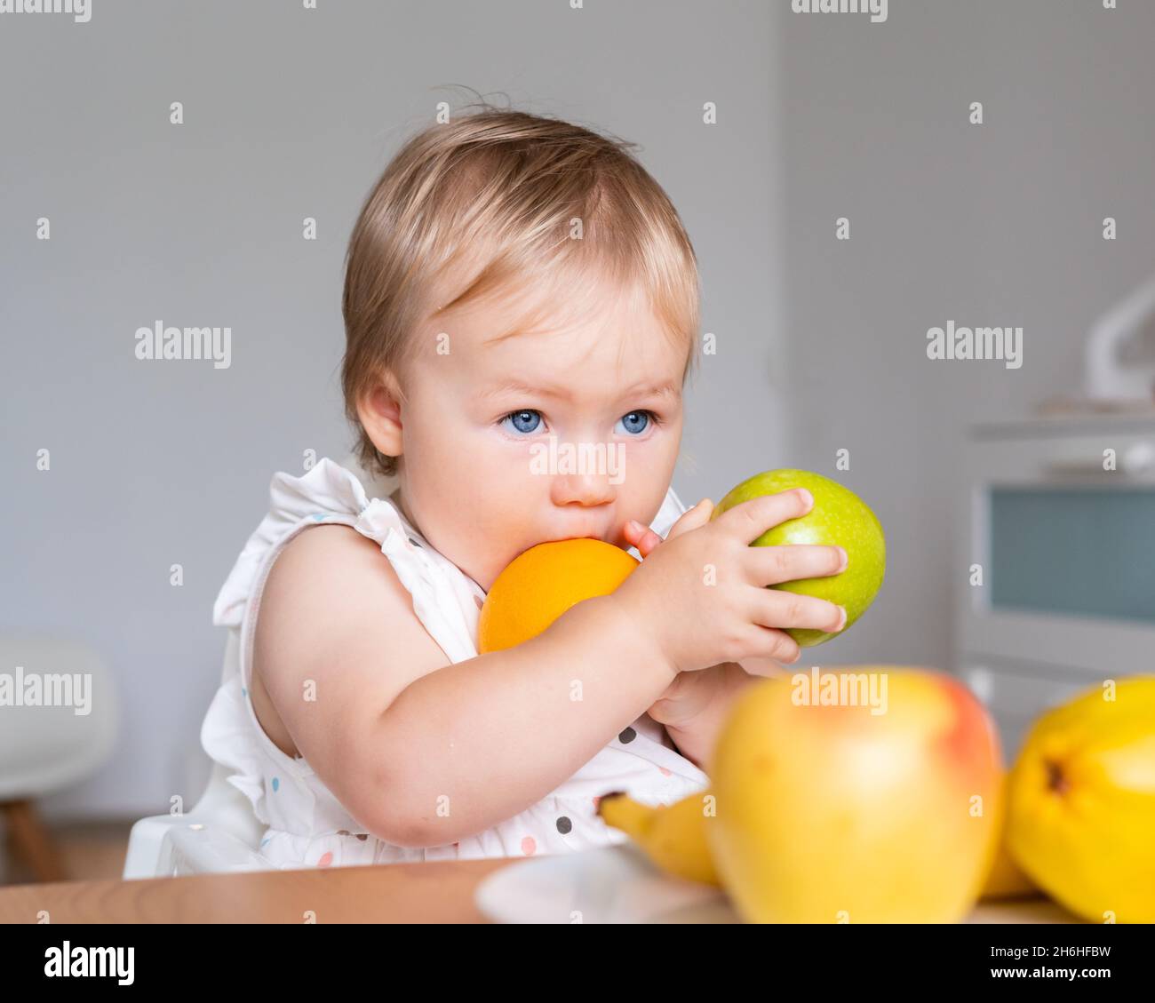 Pingelig Esser blonde blauäugige Kleinkind hält und beißt Früchte. Gesunde Essgewohnheiten. Snack für Kinder Stockfoto
