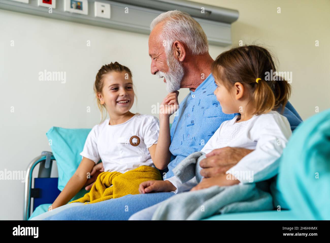 Glückliche Enkelkinder, die Großvater auf der Krankenhausstation besuchen. Support-, Familien- und Gesundheitskonzept. Stockfoto