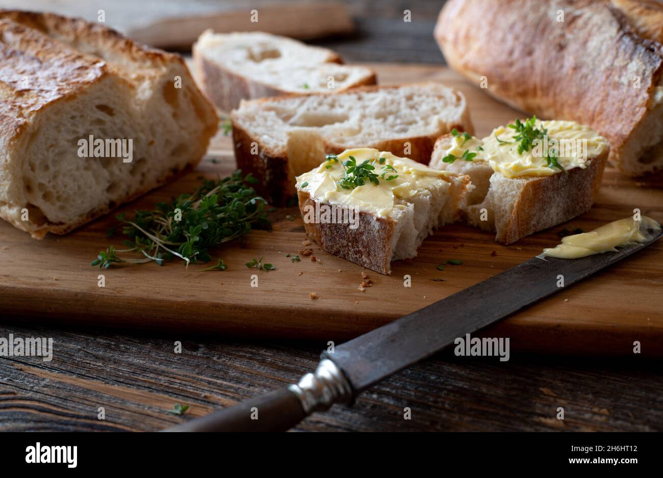 Französisches Baguette in Butterscheiben auf einem rustikalen, hölzernen Schneidebrett mit Messer Stockfoto