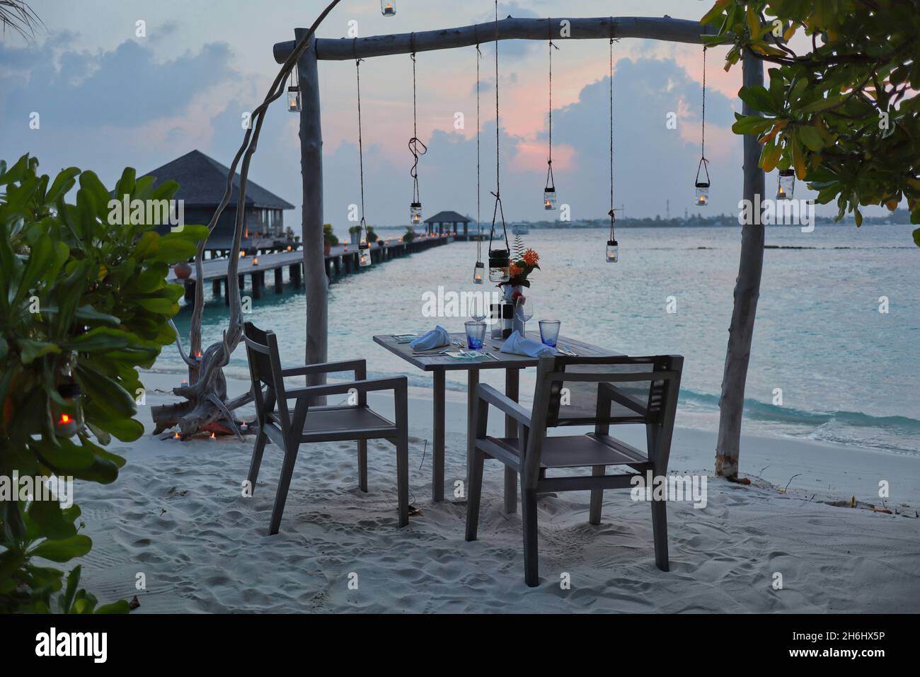 Romantisches Arrangement von Esstisch mit Stuhl am Sandstrand auf den Malediven. Wunderschöne Aussicht während der Blauen Stunde auf der Insel Malediven. Stockfoto