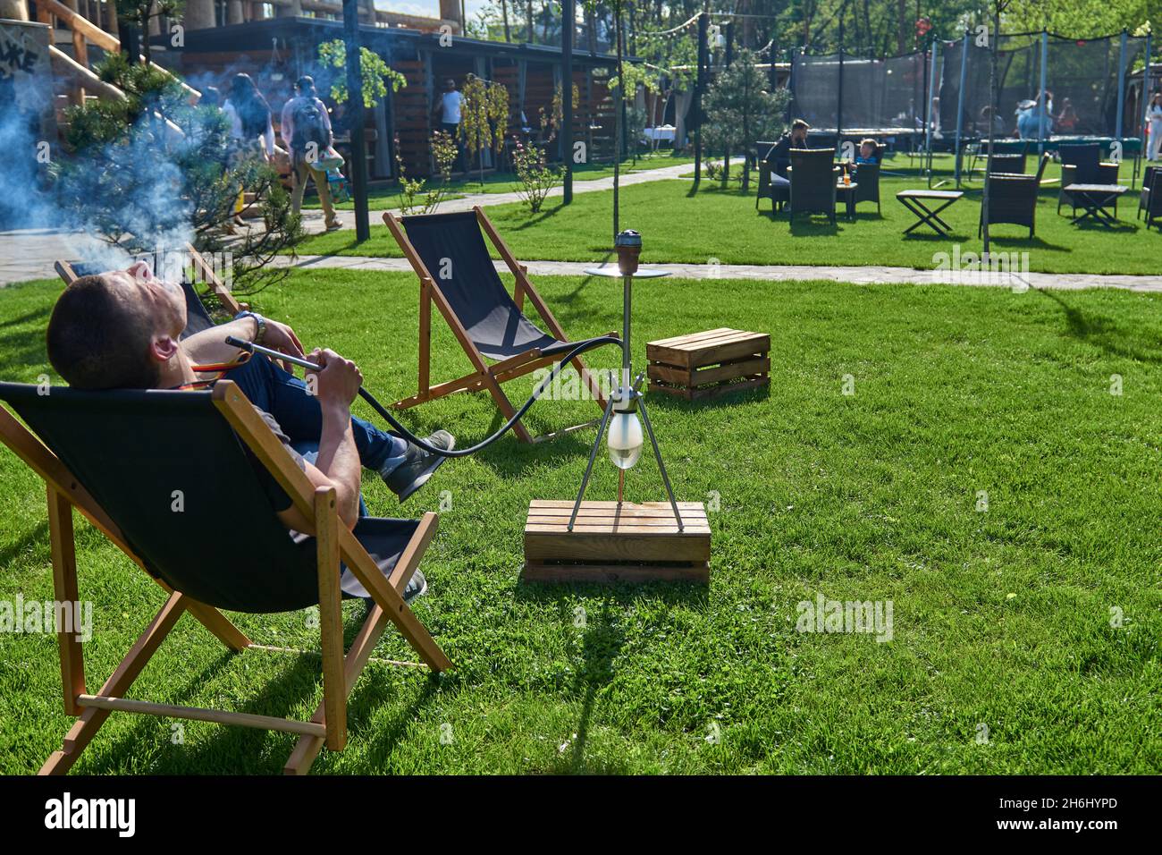Mann, der an einem warmen sonnigen Tag Shesha, Shisha-Shisha in der Natur raucht. Östlicher Shisha Rauchen, aktive Erholung an der frischen Luft. Liegestühle auf geen Gras Stockfoto