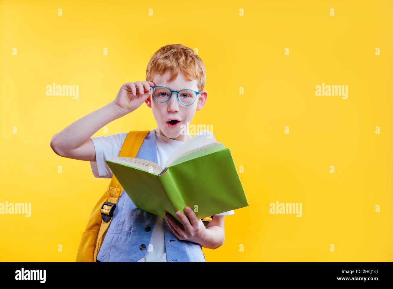 Überrascht Teenager Junge Buch lesen Blick auf die Kamera. Studio-Hochformat auf gelbem Hintergrund mit Leerzeichen für Text. Stockfoto