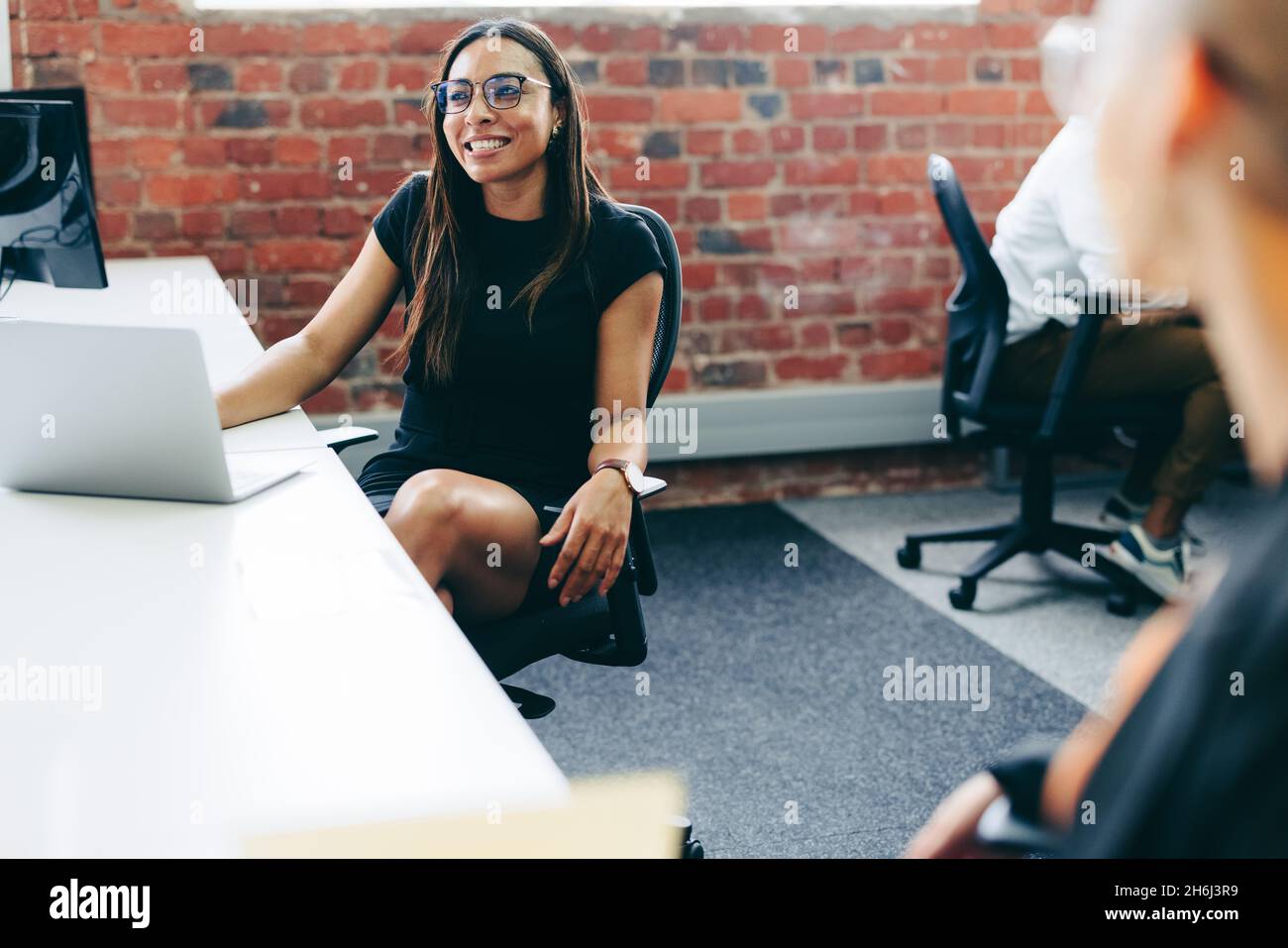 Geschäftsfrau lächelt, während sie mit ihren Kollegen im Büro arbeitet. Glückliche junge Geschäftsfrau, die in einem modernen Büro Ideen mit ihren Kollegen teilt. Stockfoto