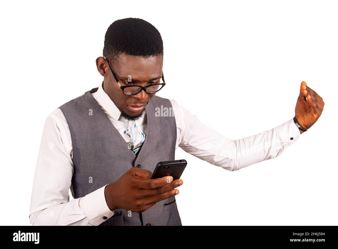 Ein hübscher junger Geschäftsmann, der eine graue Weste und eine Brille mit einem Mobiltelefon trägt, während er seinen Arm gestikuliert Stockfoto