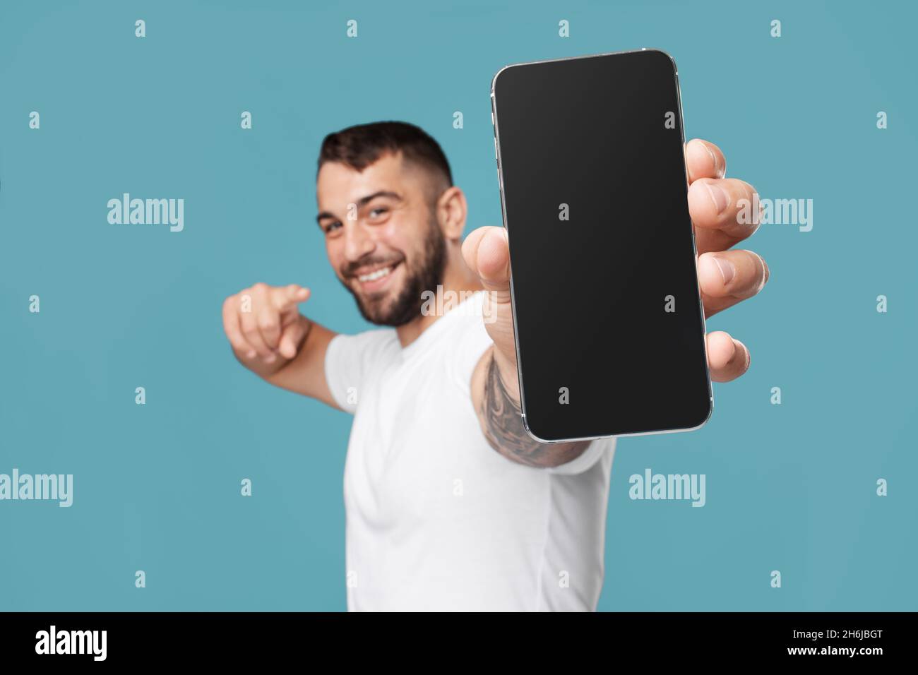 Lächelnder erwachsener europäischer Mann zeigt Finger am Telefon mit leerem Bildschirm und empfiehlt Gadget Stockfoto