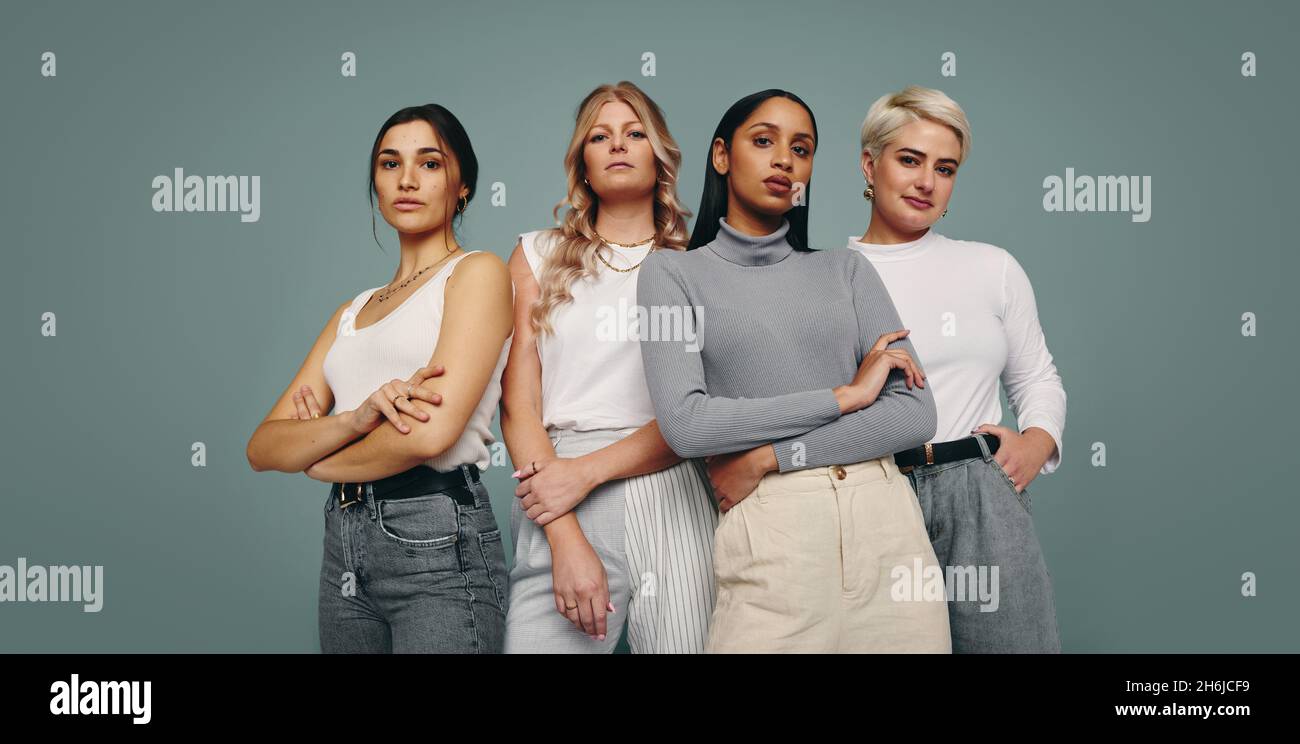 Eine Gruppe modischer Frauen, die in einem Studio zusammenstehen. Verschiedene Frauen, die vor einem Studiohintergrund auf die Kamera blicken. Vier Weibchen Stockfoto