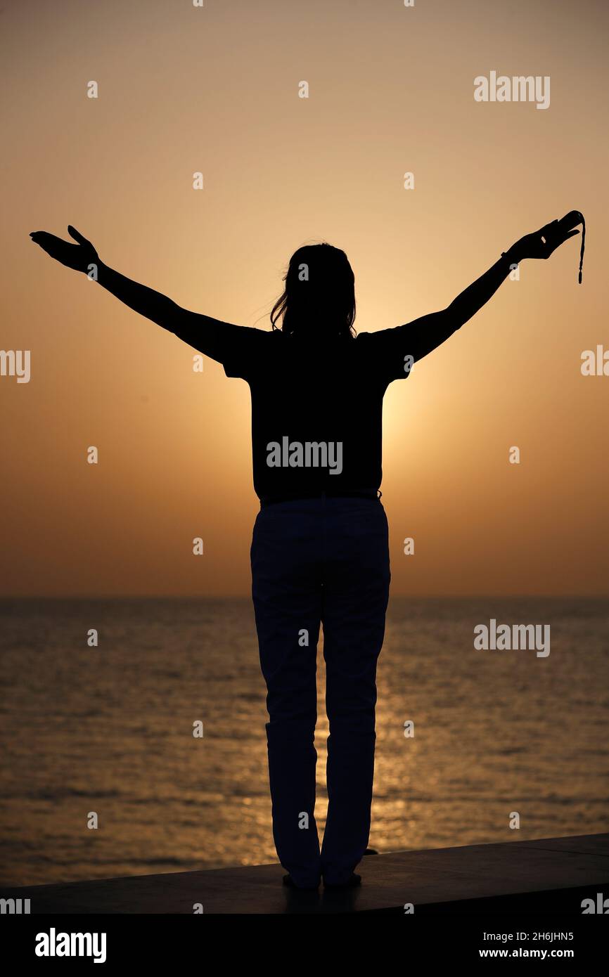 Silhouette einer treuen Frau, die bei Sonnenuntergang mit Rosenkranz als Konzept für Religion, Glauben, Gebet und Spiritualität betet, Dubai, Vereinigte Arabische Emirate Stockfoto