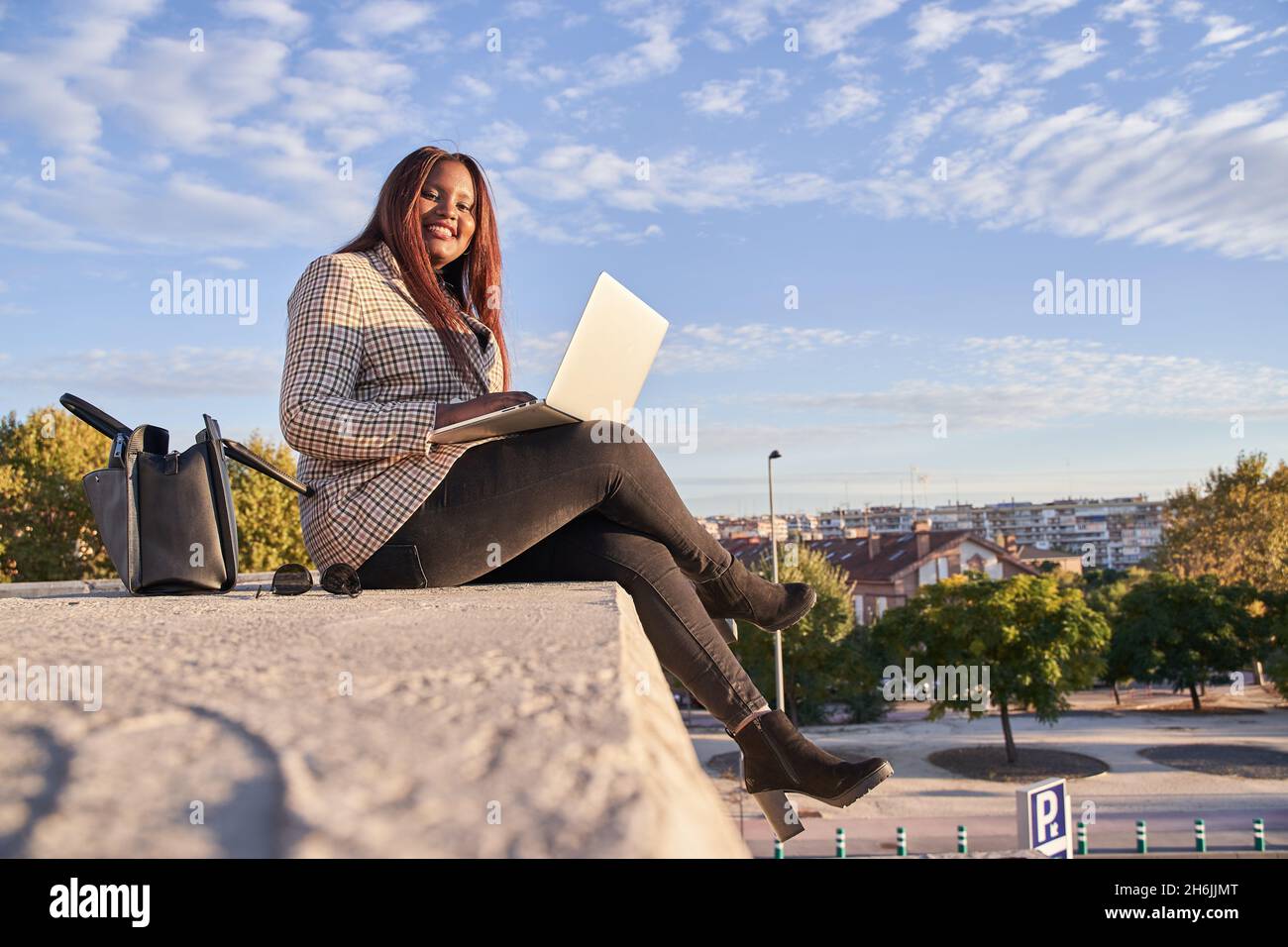 Junge afroamerikanische Frau, die im Freien sitzt und an einem Laptop arbeitet Stockfoto