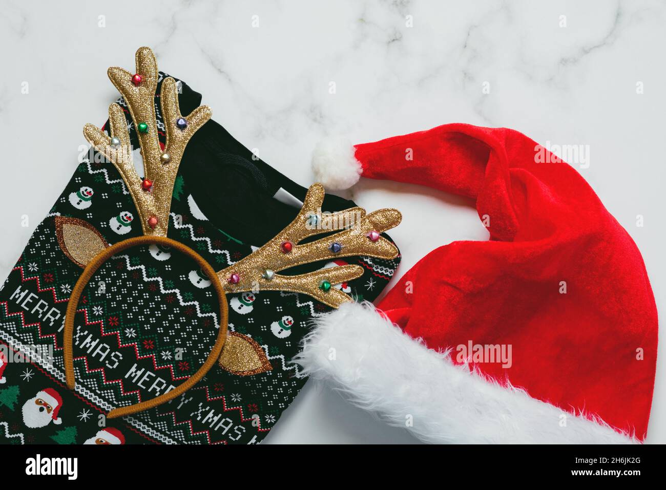 Frohe Weihnachten. Draufsicht auf weihnachts-Pullover mit hellen weihnachts-Spielzeug-Hirschgeweih und Weihnachtsmann-Hut auf einem Marmortisch Stockfoto