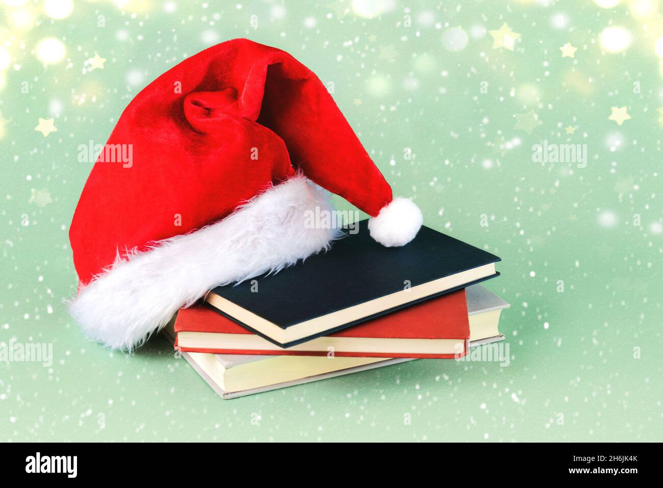 Frohe Weihnachten. Weihnachtsmann Hut mit Büchern und Weihnachtsbeleuchtung auf grünem Hintergrund. Weihnachten Konzept Hintergrund Stockfoto