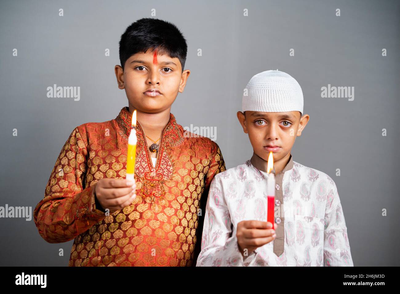 Hinduistisch-muslimische Kinder trauern oder beten, indem sie Kerzen halten, indem sie die Kamera betrachten - Konzept der Anerkennung und des Schutzes vor religiösem Kommunalismus. Stockfoto