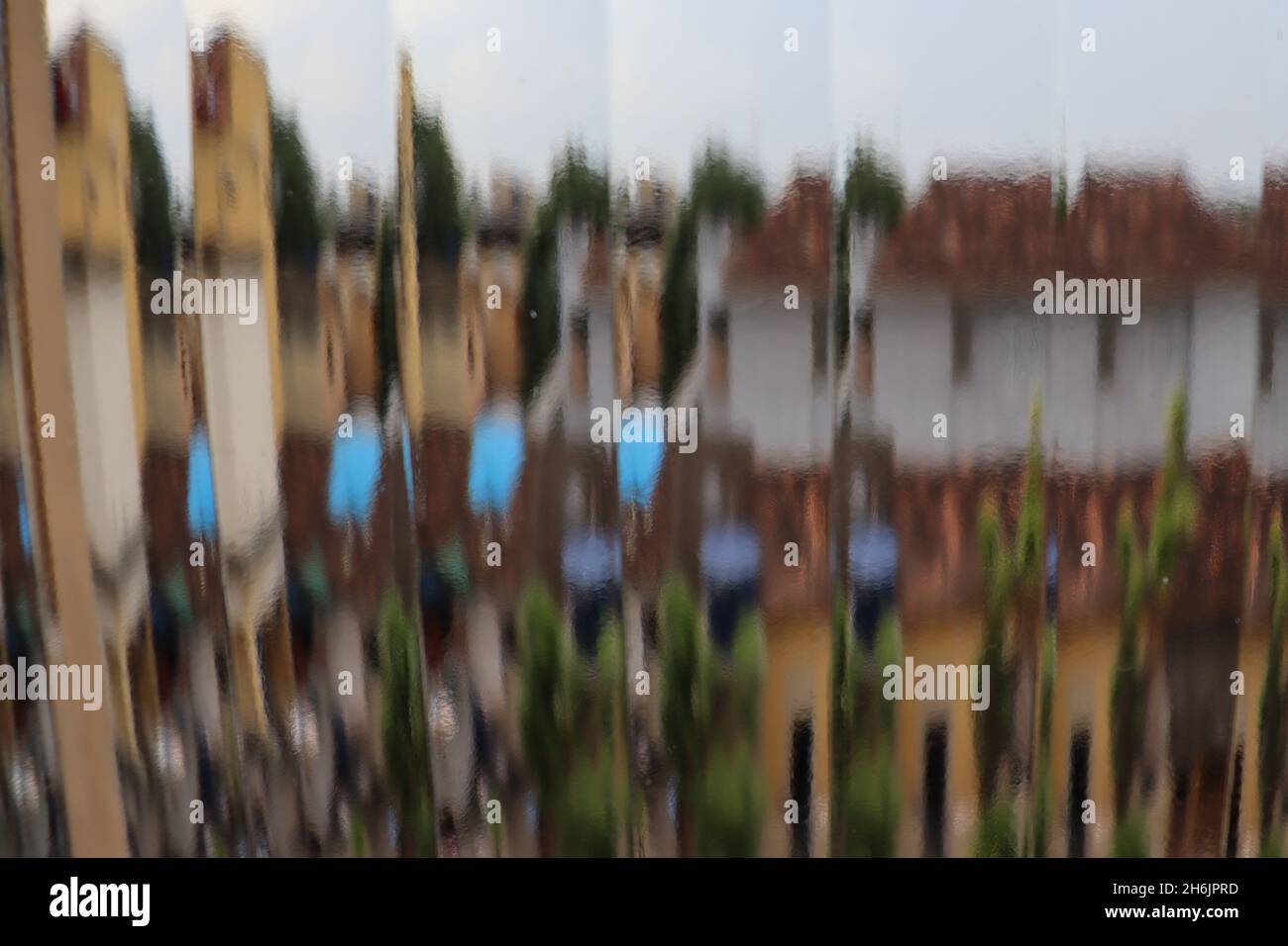 Abstrakter Blick durch ein geripptes Glasfenster, der eine fragmentierte, undefinierte Landschaft mit Häusern und Bäumen zeigt. Stockfoto