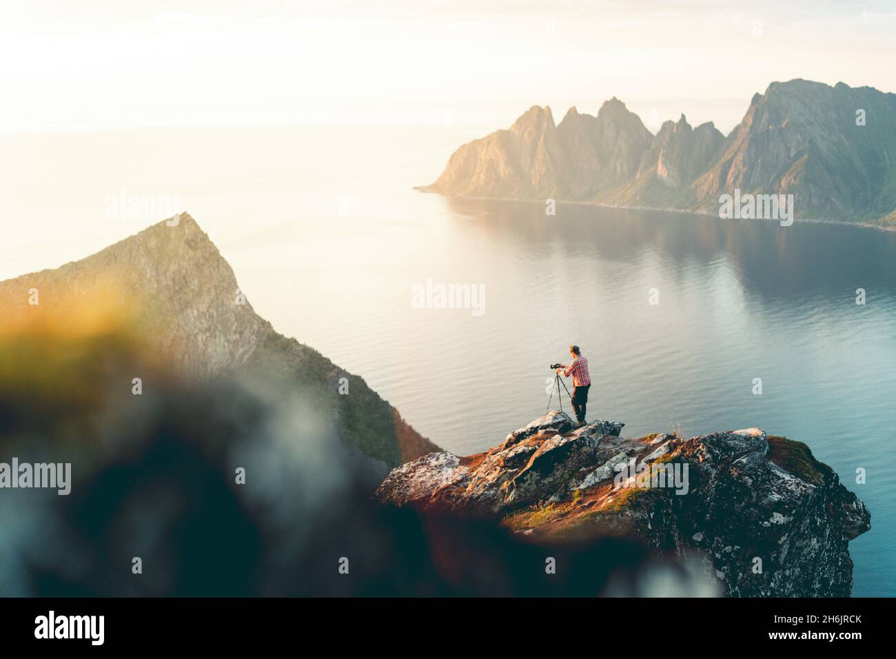 Fotograf mit Stativ auf dem Husfjellet-Berg, der den Sonnenuntergang auf den spitzen Gipfeln des Okshornan (Devil's Teeth, Senja, Norwegen, Skandinavien, Europa) beobachtet Stockfoto