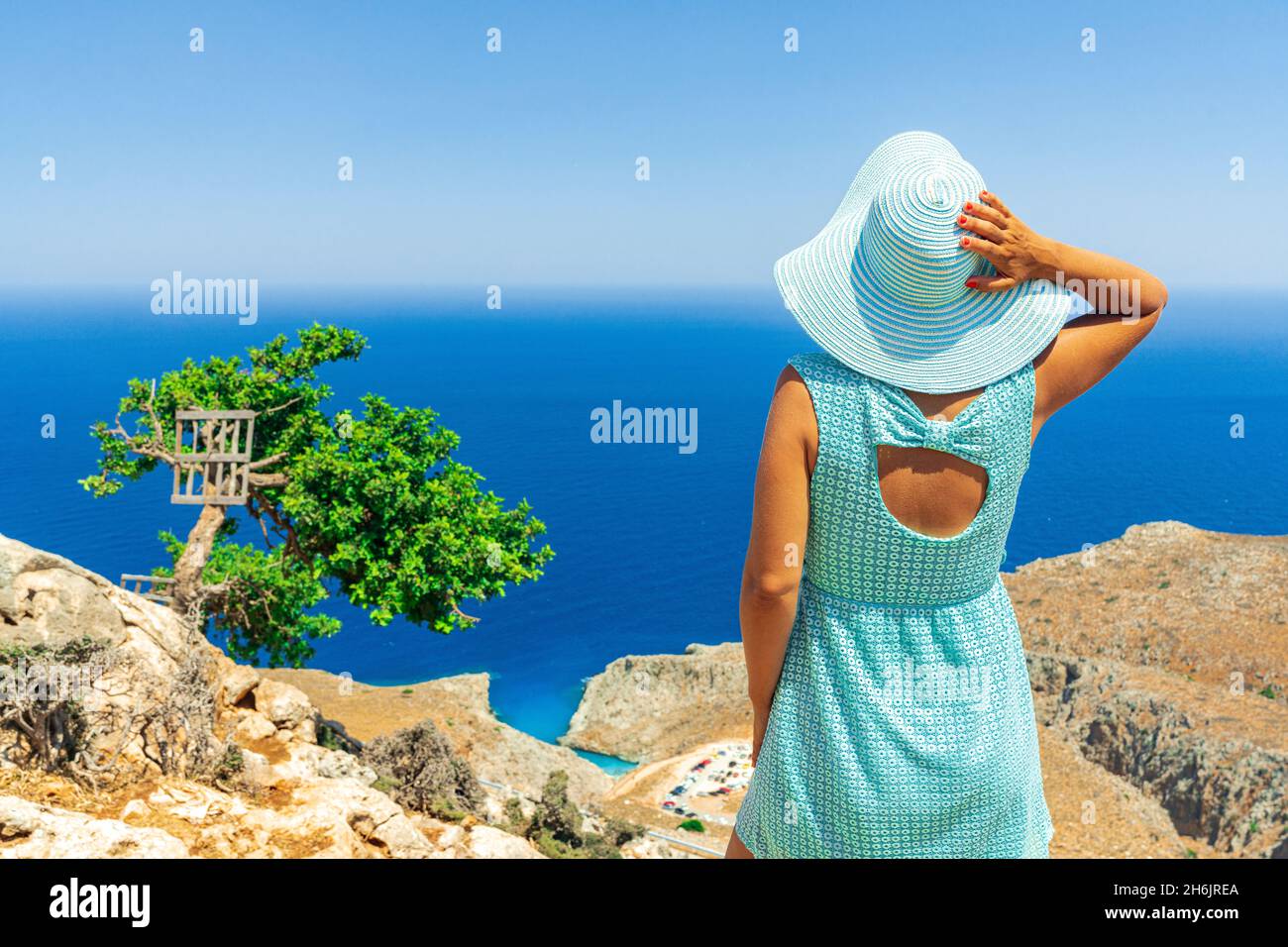 Rückansicht einer jungen Frau mit Kleid und Sonnenhut, die das Meer beobachtet, Kreta, griechische Inseln, Griechenland, Europa Stockfoto