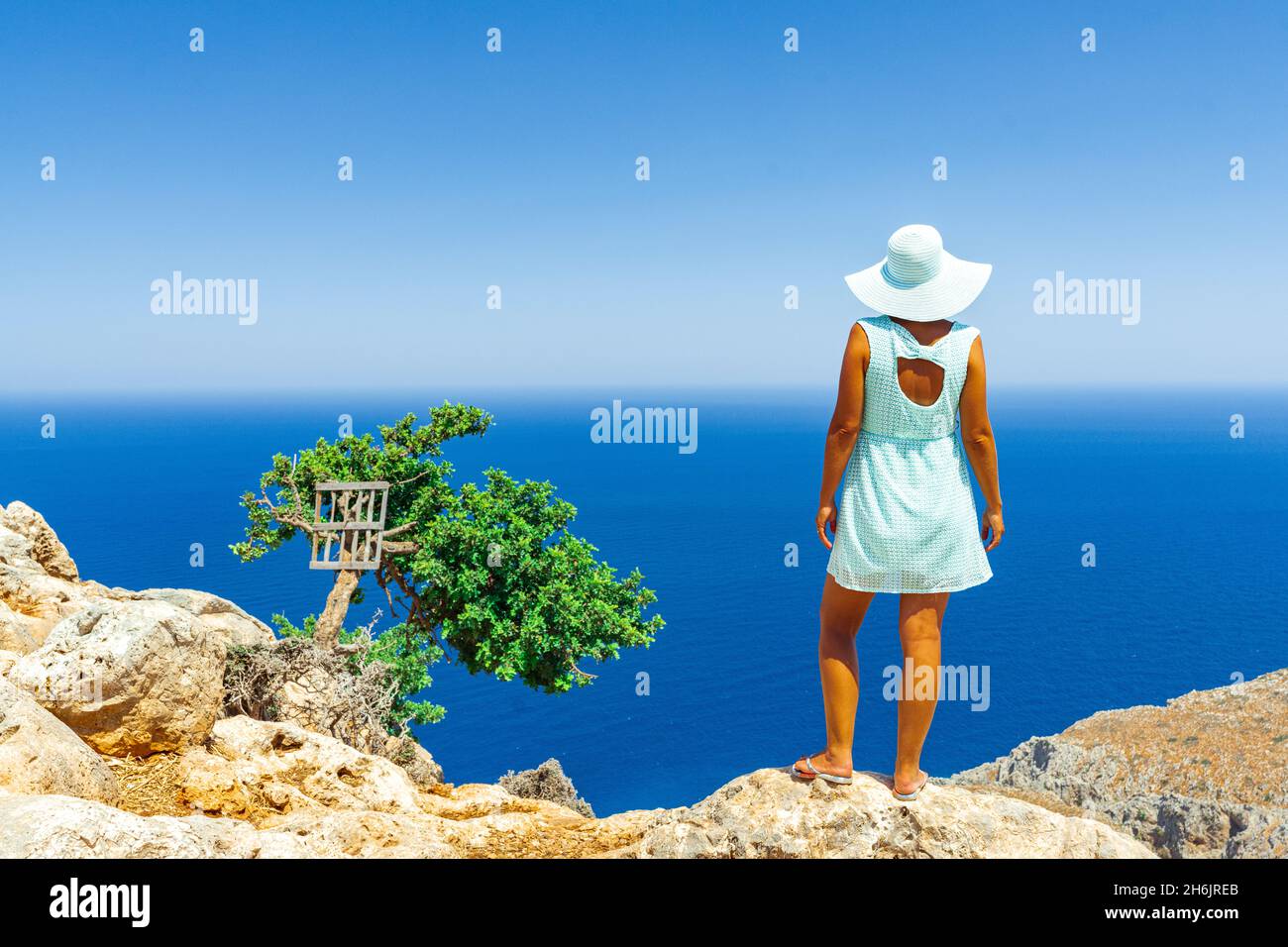 Rückansicht der Frau mit Modekleid und Hut Blick auf das Meer von Klippen, Kreta, griechischen Inseln, Griechenland, Europa Stockfoto