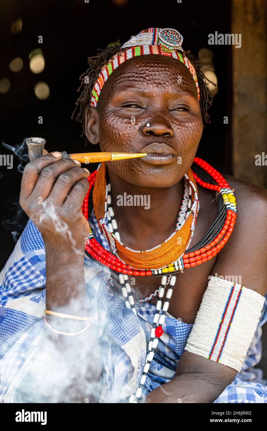 Frau mit Schönheitsnarben vom Stamm der Toposa, die eine Pfeife raucht, Eastern Equatoria, Südsudan, Afrika Stockfoto