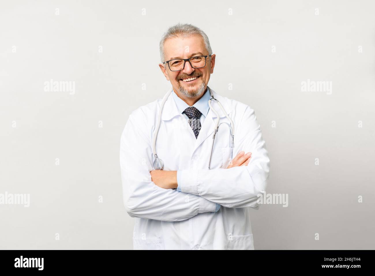 Porträt eines älteren männlichen Arztes auf weißem Hintergrund. Freundlicher Arzt, der lächelt, während er auf die Kamera schaut. Stockfoto
