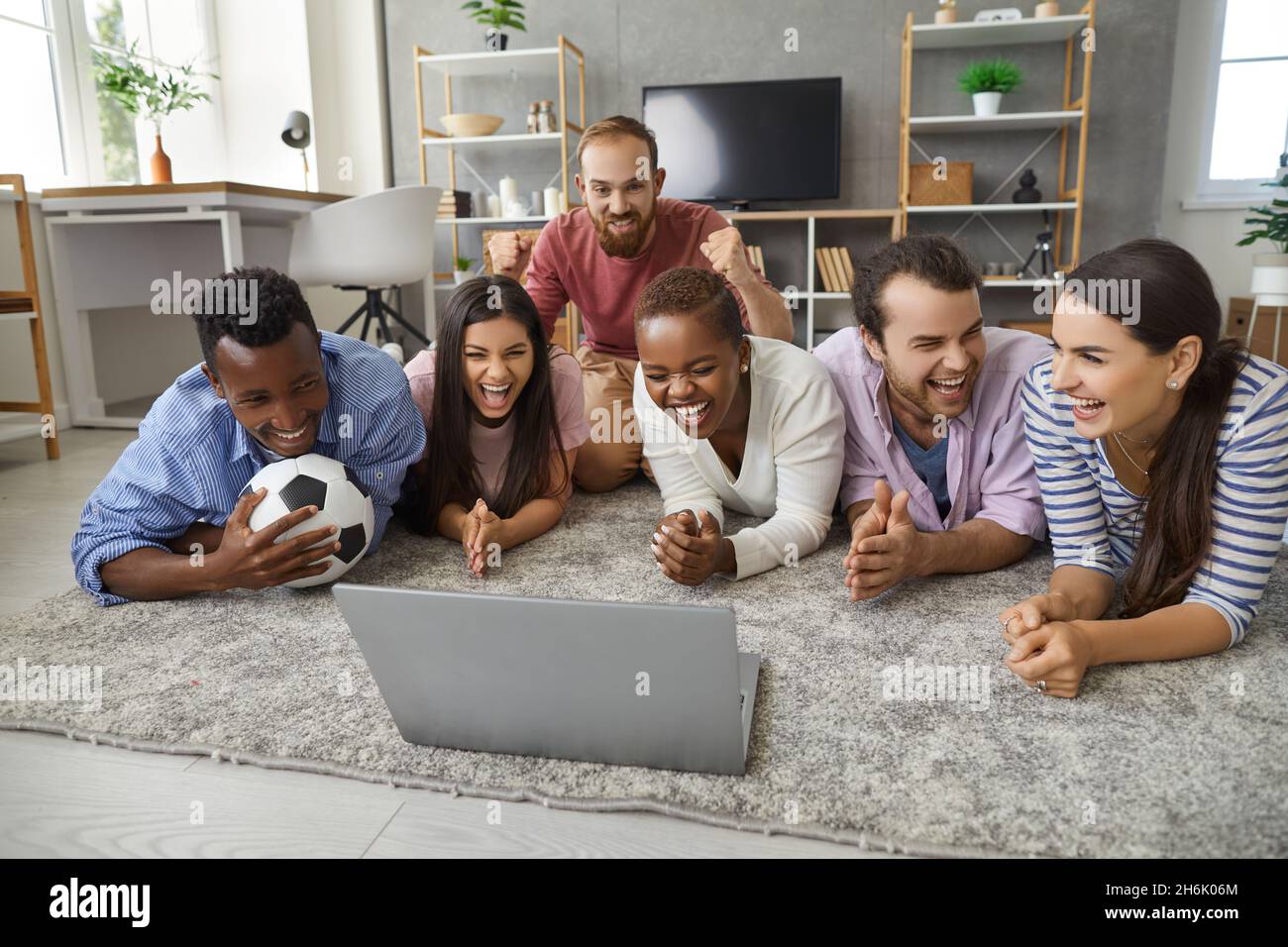 Fröhliche Freunde, eine vielfältige Gruppe, die Fußballspiele auf einem Laptop auf dem Boden beobachtet Stockfoto