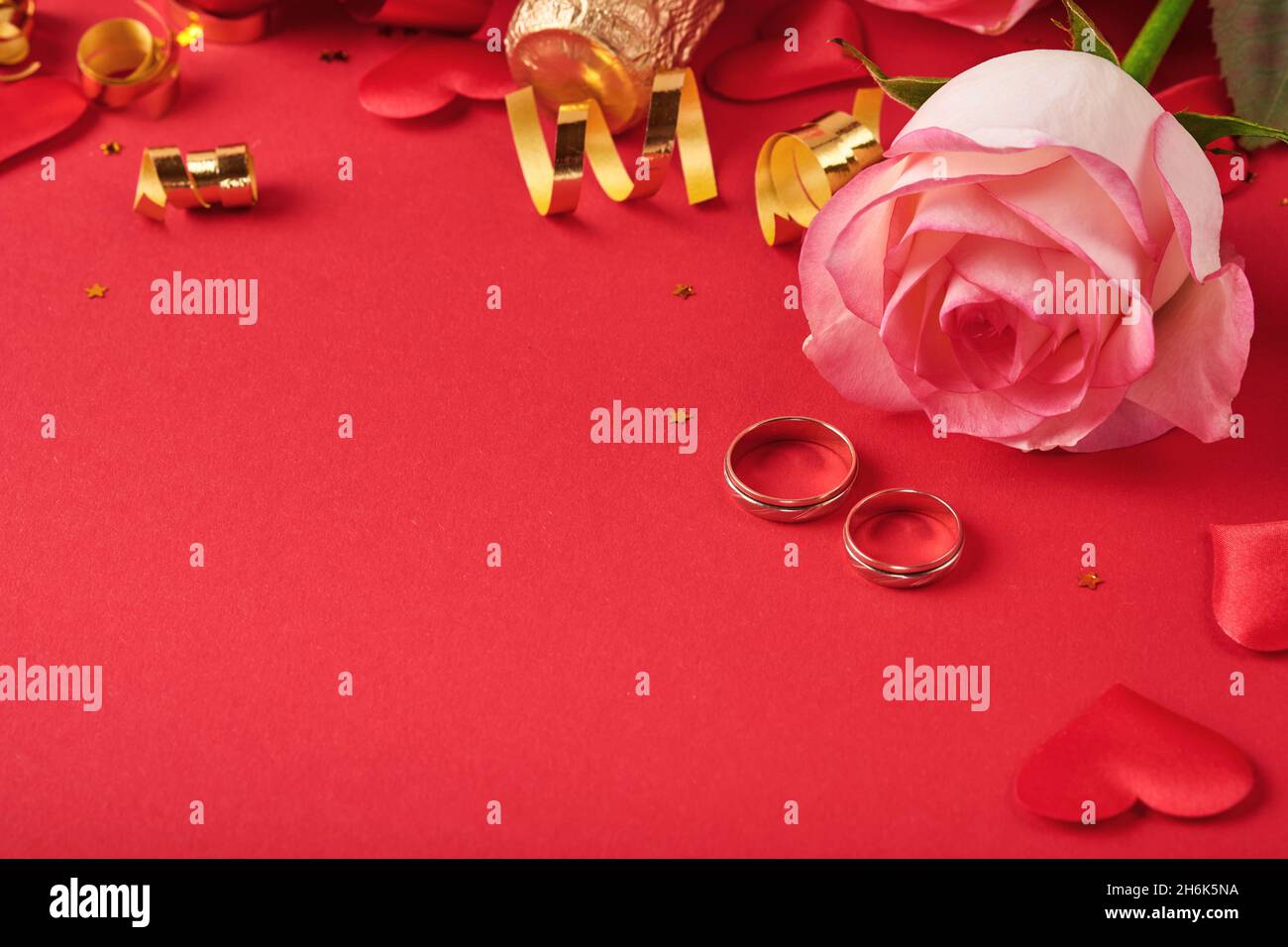 Rosa Rosen Blumen, Eheringe, Champagner, Geschenk, goldene Bänder und Konfetti Herzen auf rotem Hintergrund. Draufsicht mit Platz für Begrüßungen. Valentinstag Stockfoto