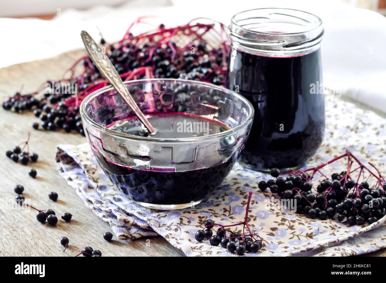 Hausgemachter schwarzer Holunderbeersirup in Glasschüssel und Glas und Trauben schwarzer Holunderbeere im Hintergrund Stockfoto