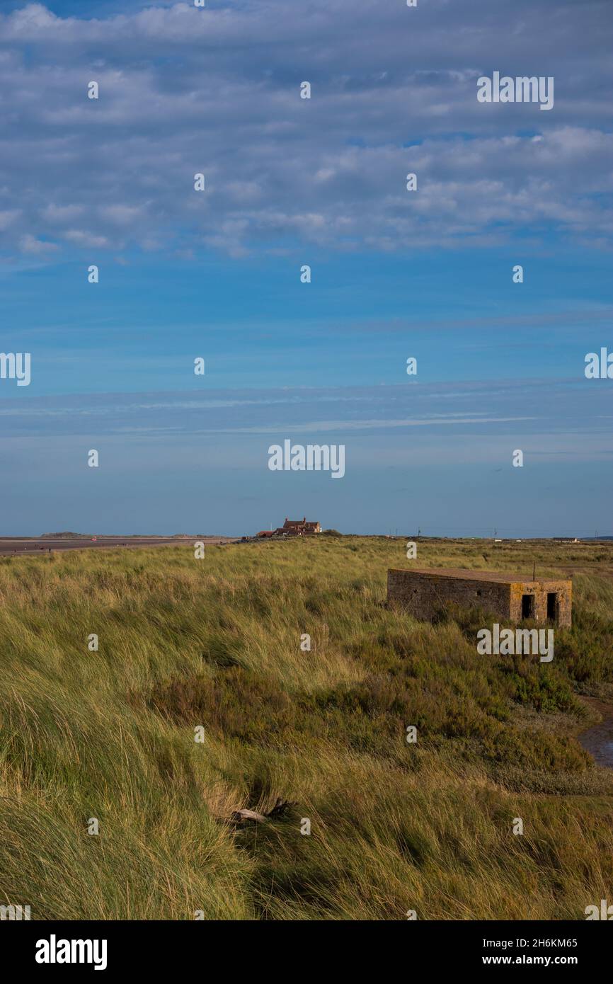 Alte Pillenbox aus dem Zweiten Weltkrieg zwischen den Dünen neben Salzsumpfgebieten am Brancaster Beach im Norden Norfolks in England Stockfoto