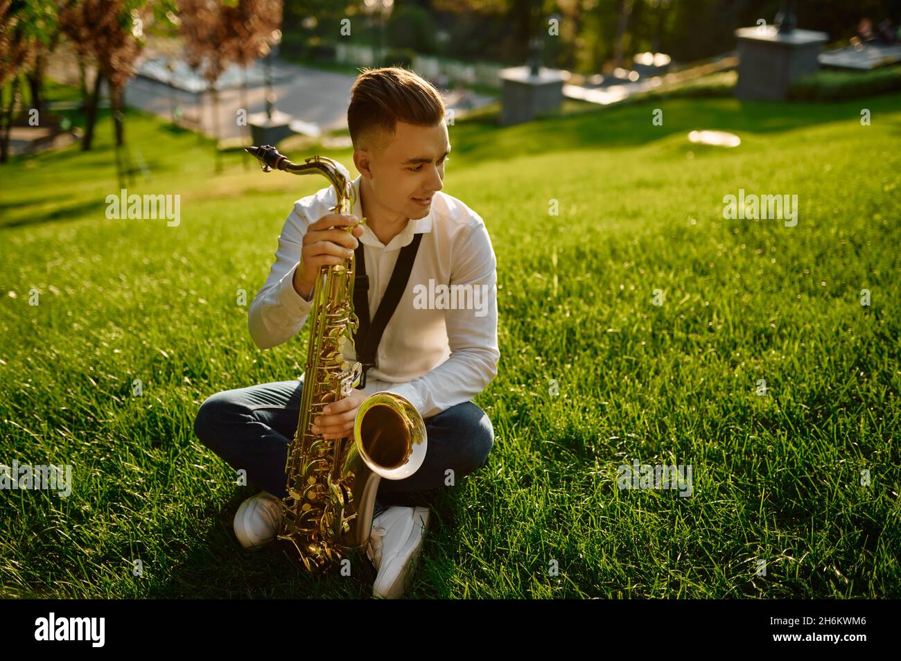 Junger Saxophonist mit Saxophon auf Gras sitzend Stockfoto