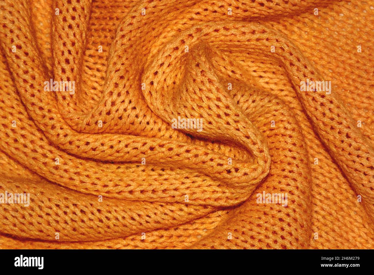 Struktur eines warmen orangefarbenen Strickpullovers mit Falten. Zöpfe im Muster, weicher Fokus. Flacher Style, Nahaufnahme. Stockfoto