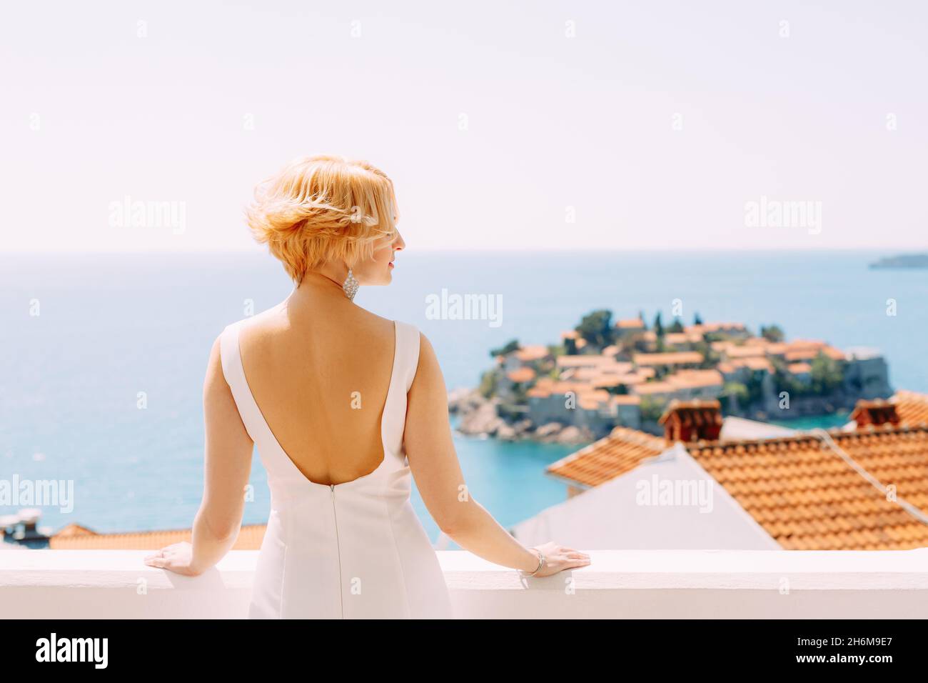 Die Braut im weißen Kleid steht seitlich und blickt auf die Insel Sveti Stefan bei Budva, Montenegro. Rückansicht. Nahaufnahme Stockfoto