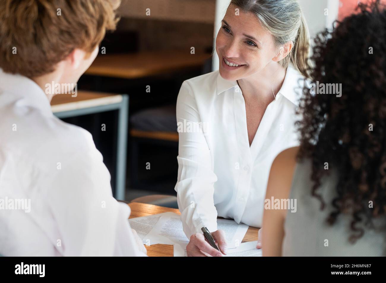 Lächelnde reife Frau im Gespräch mit einem jungen Paar im Büro Stockfoto