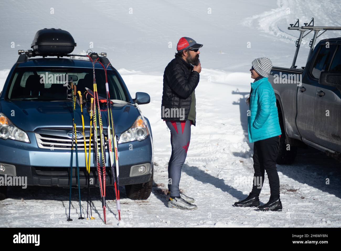 Ein Mann und eine Frau im Gespräch stehen auf einem schneebedeckten Parkplatz von Angesicht zu Angesicht mit ihrem Auto und Lastwagen. Stockfoto