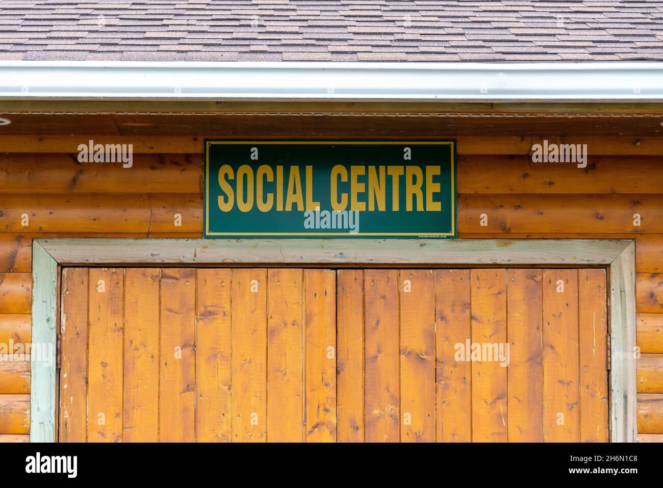 Ein Gebäude mit orangefarbenem Holzbalken und einem Schild mit den Worten Sozialzentrum hing über doppelten Holztüren. Das Schild ist grün mit gelbem Schriftzug Stockfoto