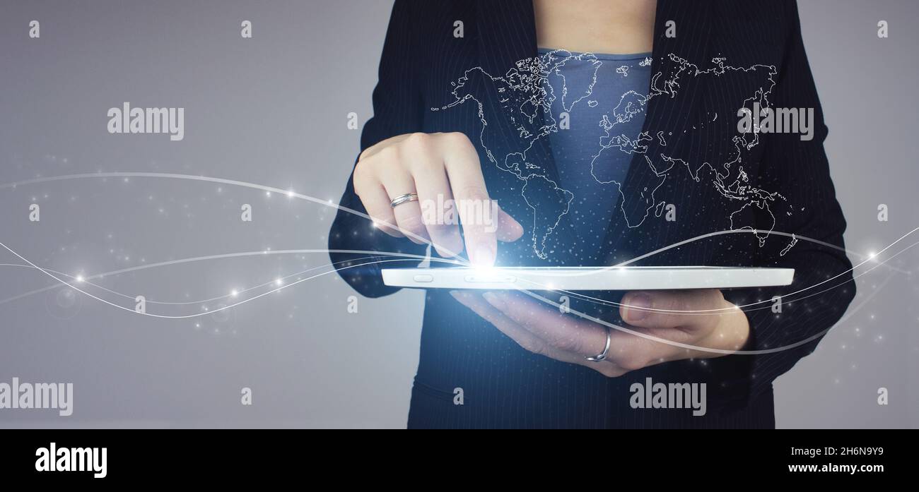Medien weltweit Technologiekonzept. Weiße Tablette in Geschäftsfrau Hand mit digitalen Hologramm Weltkarte Zeichen auf grauem Hintergrund. Internationale Geschäfte Stockfoto